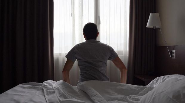 Silhouette of lonely man sitting on bed in dark room by bedroom window. Depressed, early morning wake up, lazy, tired concepts