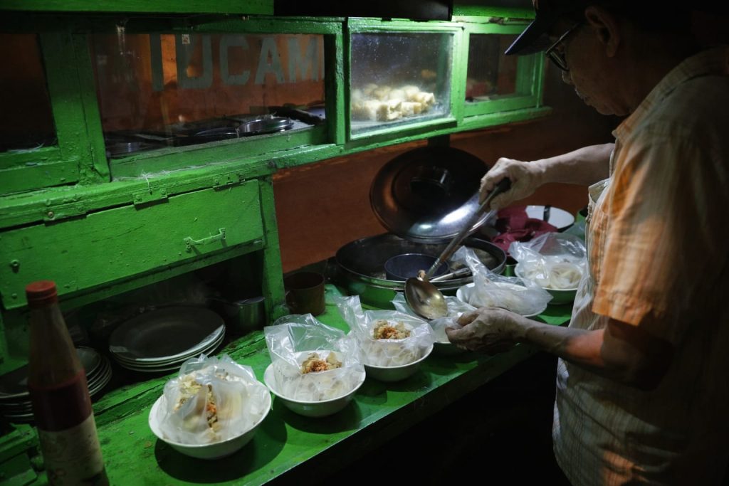 Puluhan Tahun Tak Berubah, Tahu Campur Rp5 Ribu di Mojokerto Tetap Laris Pedagang meracik tahu campur dagangannya di gerobak sederhana depan SMA Jayanegara, Mojokerto, (Foto: Dian)