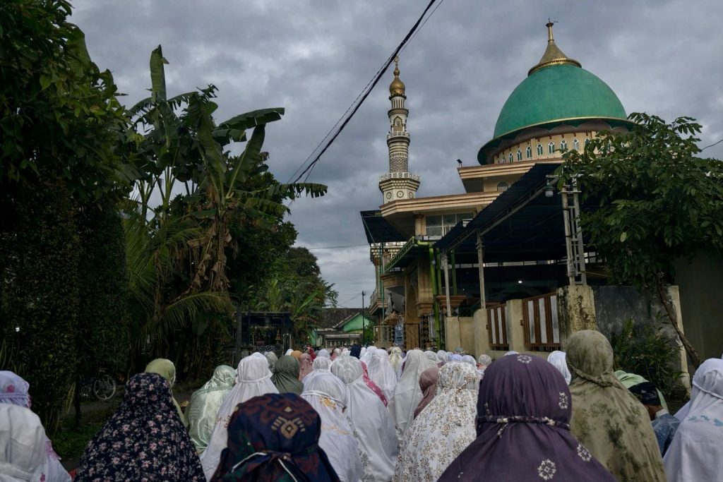 [07.43, 21/3/2026] Mjk Rahma IK'23: Di Bawah Langit Mendung, Sholat Ied di Grogol Kutorejo Tetap Khusyuk Langit mendung menggantung di atas Masjid Grogol, Kutorejo, Sabtu (21/3/2026) pagi. Di tengah suasana yang teduh itu, ratusan jamaah tetap memadati area masjid untuk melaksanakan Sholat Ied dengan khusyuk, meski gerimis sempat turun tipis. Sejak subuh, awan kelabu telah menyelimuti kawasan tersebut. Namun kondisi cuaca tak menyurutkan langkah warga yang datang bersama keluarga untuk menunaikan ibadah di hari kemenangan. Hamparan sajadah terbentang hingga ke halaman masjid. Sejumlah jamaah tampak membawa payung sebagai antisipasi hujan, sementara yang lain tetap duduk tenang mengikuti rangkaian ibadah. Takbir berkumandang dengan syahdu, berpadu dengan udara pagi yang sejuk. Suasana yang biasanya diselimuti terik matahari justru terasa lebih nyaman, membuat jamaah dapat beribadah dengan lebih khusyuk. “Alhamdulillah, walaupun mendung tapi lebih adem, jadi ibadah terasa lebih tenang,” ujar Vina (27), salah satu jamaah. Hal serupa disampaikan Candra (22), warga setempat. Ia mengaku sempat khawatir hujan akan turun lebih deras saat pelaksanaan sholat. “Tadi sempat gerimis, tapi tidak lama. Kami tetap bisa mengikuti sholat dengan lancar sampai selesai,” katanya. Di sela-sela jamaah, anak-anak tampak ceria mengenakan pakaian terbaik mereka. Sementara para orang tua saling bersalaman usai sholat, menambah hangat suasana kebersamaan di pagi hari raya. Mendung yang menaungi langit pagi itu tak hanya menghadirkan kesejukan, tetapi juga memperkuat rasa kebersamaan di antara jamaah yang hadir, mengiringi Hari Raya dengan penuh syukur. [07.43, 21/3/2026] Mjk Rahma IK'23: Jamaah melaksanakan Sholat Ied di Masjid Grogol, Kutorejo, Sabtu (21/3/2026) pagi di bawah langit mendung. (Rahma)