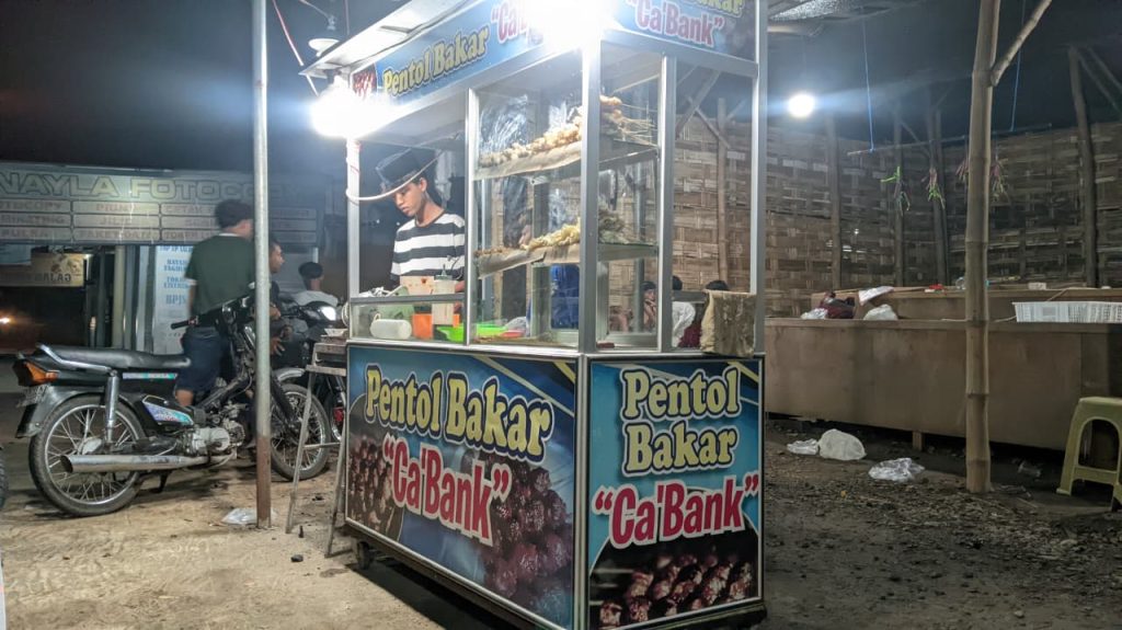 Pentol Bakar Ca’Bank, Usaha Remaja Karang Taruna Raup Ratusan Tusuk Sejumlah remaja Karang Taruna Dusun Modongan melayani pembeli di lapak Pentol Bakar Ca’Bank yang dikelola secara bersama sebagai upaya pemberdayaan ekonomi anak muda desa. (Foto: Dian Wahyu)