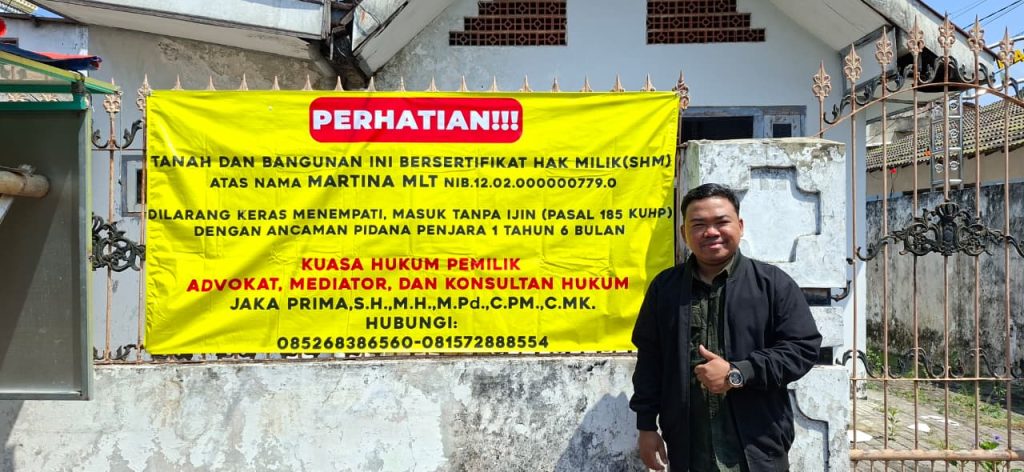 Jaka Prima, S.H., M.H., M.Pd., selaku kuasa hukum pemilik, berpose di depan bangunan yang dipasangi spanduk pemberitahuan terkait status kepemilikan properti di Kota Mojokerto